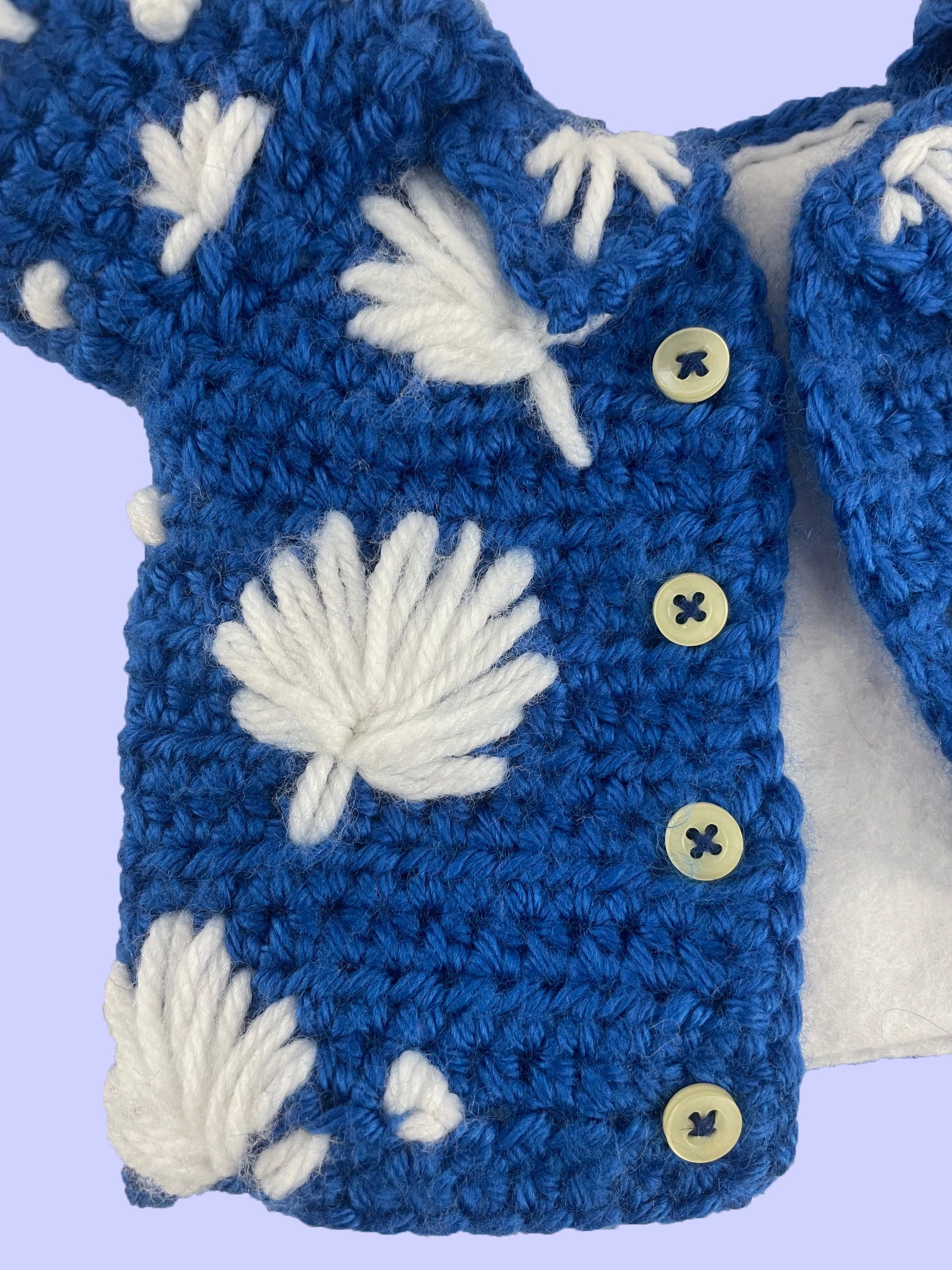 Close-up of crochet plush shirt showing functional buttons and hand-stitched white flower details on blue fabric.