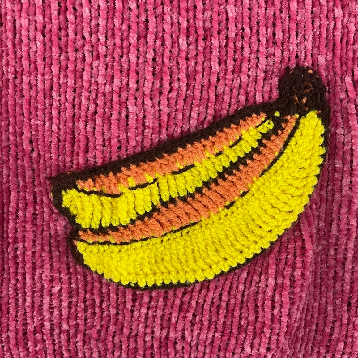 Close-up of yellow crochet banana applique stitched onto pink knit fabric